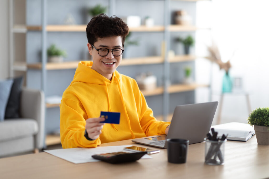 Smiling asian guy using credit card and pc